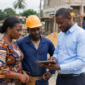 Client, artisan et représentant TEMG consultant une tablette sur un chantier à Libreville, illustrant les évolutions apportées par la plateforme au Gabon.